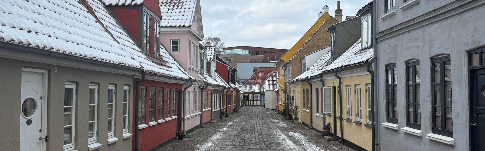 A row of colorful houses on a cobblestone street with a dusting of snow. 